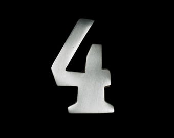 May include: A silver-colored number four against a black background. The number has a slightly textured surface and a modern, angular design. The lighting highlights the shape and form of the numeral.