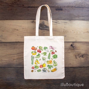 Könnte beinhalten: Eine weiße Einkaufstasche mit einer bunten Illustration verschiedener Gemüse und Früchte, darunter Karotten, Tomaten, Paprika und Kirschen. Die Tasche trägt den Text "illuboutique" unten aufgedruckt.