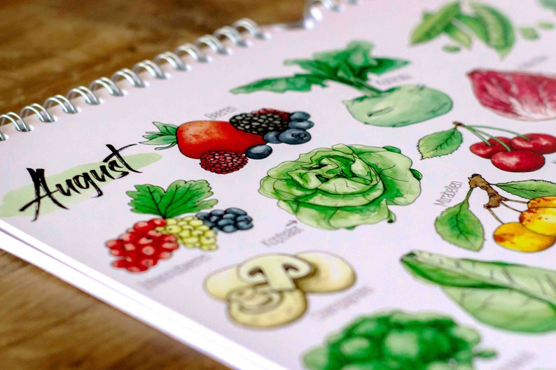 May include: A calendar page for August with watercolor illustrations of seasonal fruits and vegetables. The page features a pink background with the word "August" written in black cursive. The illustrations include strawberries, blueberries, raspberries, red currants, white currants, mushrooms, lettuce, kohlrabi, cherries, and apples.