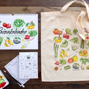 Könnte beinhalten: Ein Set aus drei Artikeln für einen saisonalen Lebensmittelkalender: ein Kalender mit Aquarell-Illustrationen von Obst und Gemüse, eine Einkaufstasche mit ähnlichem Design und ein leeres Notizbuch mit einer Schwarzweiß-Illustration einer Brombeere.