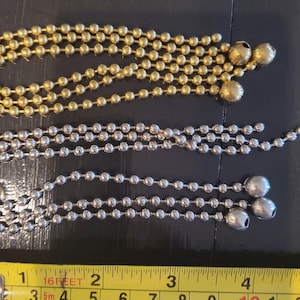 May include: Two strands of chain, one gold and one silver, with a measuring tape in the foreground. The gold chain has five strands and the silver chain has three strands. The measuring tape is marked in feet and inches.