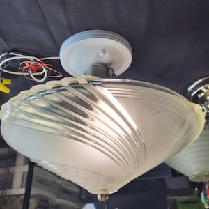 May include: Vintage ceiling light fixture with a white and frosted glass shade. The shade has a unique, swirled design and is attached to a white ceiling mount. The fixture is designed to be mounted flush against the ceiling.