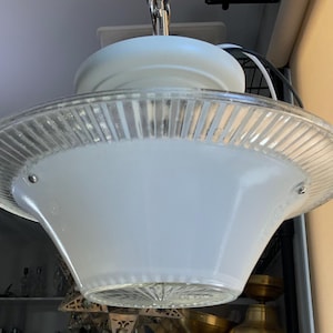 May include: A ceiling pendant light fixture featuring a wide, frosted white glass bowl shade with a clear, vertically ribbed glass rim. The fixture includes a central white canopy and a clear, starburst-patterned glass base at the bottom.