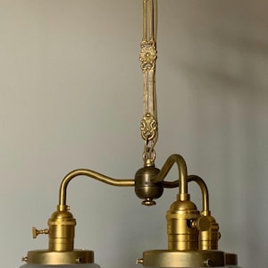 May include: A brass ceiling light fixture featuring a decorative chain and canopy, a central hub, and two downward-facing light sockets. Each socket holds a fluted, frosted glass shade with a clear vertical ribbed pattern and a brass metal rim.