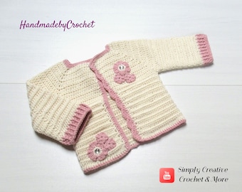 May include: A crocheted baby cardigan in cream with pink trim and pink crocheted flowers with a rhinestone center. The cardigan is laid flat on a white surface. HandmadebyCrochet is written in purple text at the top of the image. Simply Creative Crochet & More is written in red text at the bottom of the image.
