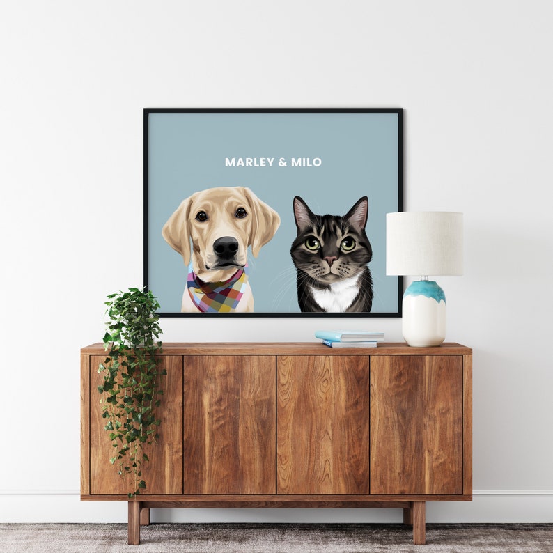 May include: A framed print featuring a golden Labrador Retriever wearing a colorful bandana and a gray tabby cat. The text "MARLEY & MILO" is displayed in white on a light blue background. The artwork is displayed on a wooden cabinet.