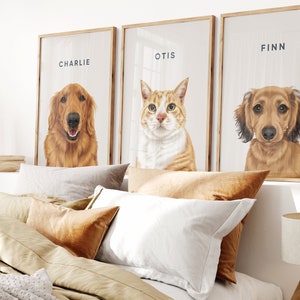 May include: Three framed pet portraits featuring a Golden Retriever named Charlie, an orange tabby cat named Otis, and a Dachshund named Finn. The portraits have wooden frames and are displayed above a bed with pillows.
