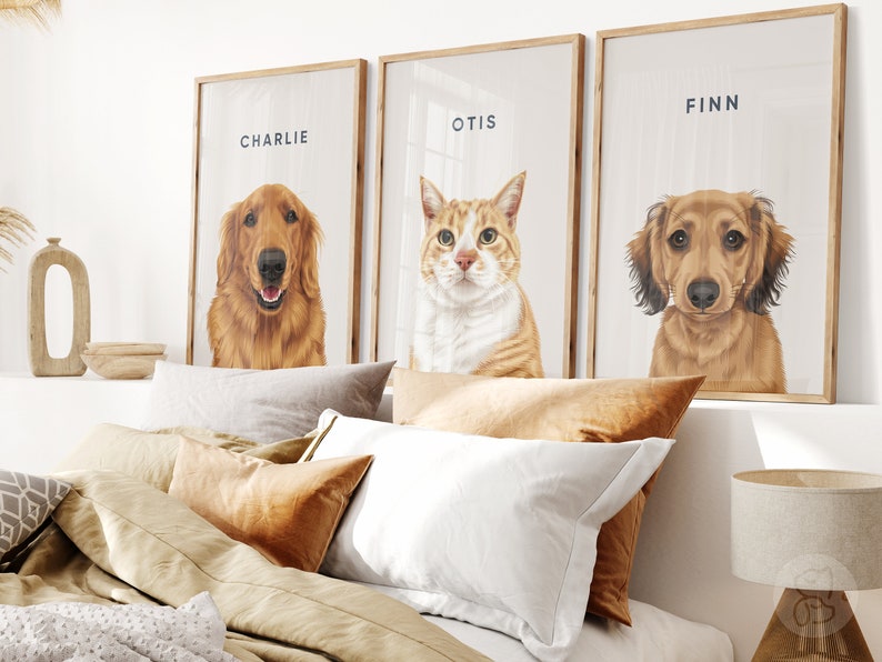 May include: Three framed pet portraits featuring a Golden Retriever named Charlie, an orange tabby cat named Otis, and a Dachshund named Finn. The portraits have wooden frames and are displayed above a bed with pillows.