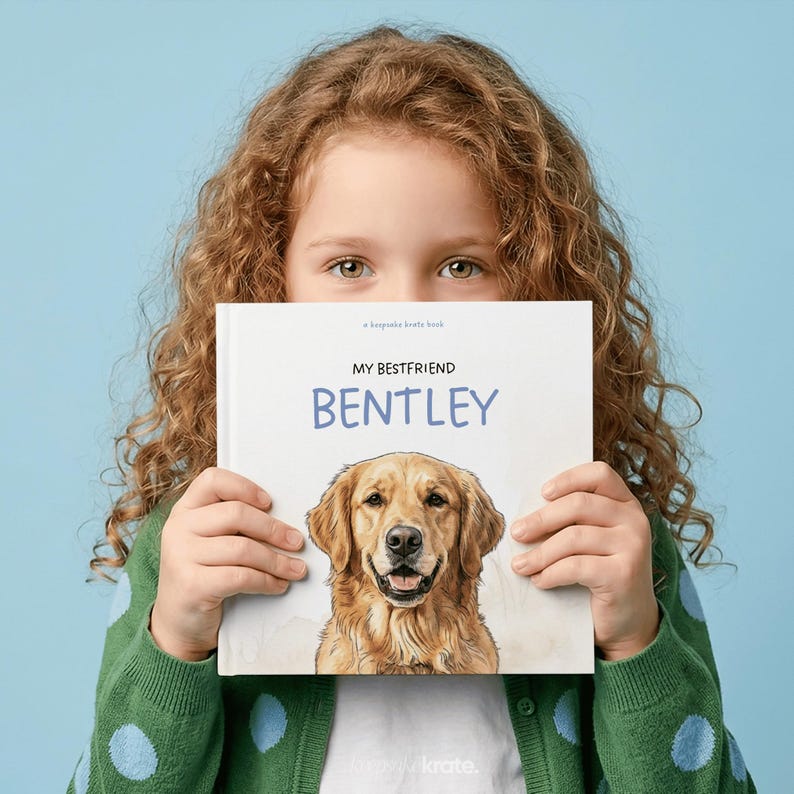 Może przedstawiać: Kwadratowa książka w twardej oprawie z białą okładką przedstawiającą realistyczną ilustrację psa rasy golden retriever. Tekst na okładce brzmi "a keepsake krate book" oraz "MY BESTFRIEND BENTLEY" czarnymi i niebieskimi literami.