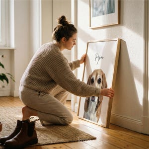May include: A framed watercolor portrait of a dog named Piper. The dog has brown and white fur and is the focal point of the artwork. The frame is a light wood color. A person is holding the framed artwork.