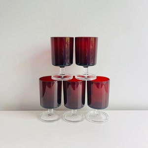Peut inclure: Six verres à pied rouge rubis vintage empilés en pyramide. Les verres ont un bol cylindrique avec des rainures verticales et une base claire et circulaire. Les verres sont disposés sur une surface blanche sur fond blanc.