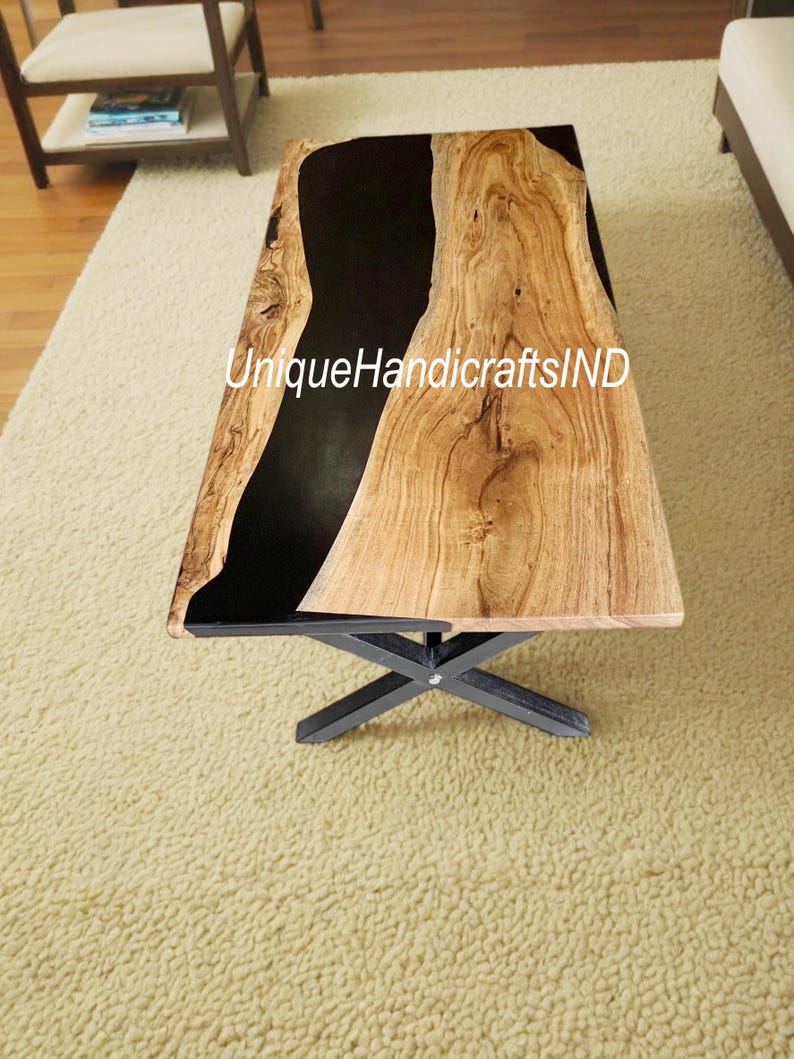 Op de afbeelding: Een rechthoekige salontafel met een blad van natuurlijk houtnerf en een zwarte epoxyharsrivier. De tafel heeft een zwart metalen onderstel. De tekst "UniqueHandicraftsIND" is zichtbaar op de tafel.