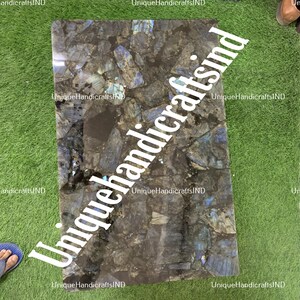 May include: A dark blue and black square tile with iridescent blue and green flecks. The tile is made of labradorite stone.