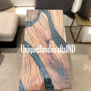 Könnte beinhalten: Ein Holz-Couchtisch mit einem Einlegeteil aus grünem Epoxidharz. Der Tisch hat eine natürliche Holzoptik und ein einzigartiges Flussdesign. Der Text "UniqueHandicraftsIND" ist auf dem Tisch sichtbar.