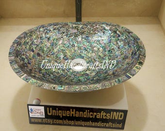 May include: Oval-shaped sink made of iridescent mother of pearl mosaic tiles. The sink is on a white pedestal with a black sign that reads "UniqueHandicraftsIND www.etsy.com/shop/uniquehandicraftsind"