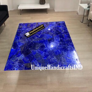 Puede incluir: Una mesa de centro cuadrada con una tapa hecha de piedra de lapislázuli azul. La mesa está hecha de muchas piezas pequeñas de piedra que se unen en un patrón de mosaico. La mesa está sobre un suelo de madera. El texto "UniqueHandicraftsIND" es visible en la mesa.