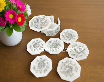 May include: Set of eight white marble coasters with intricate floral designs in silver. The coasters are octagonal and come in a matching box.