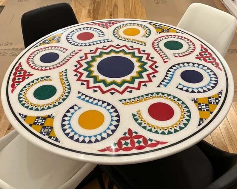 Puede incluir: Una mesa redonda blanca con un dise&ntilde;o geom&eacute;trico colorido. El dise&ntilde;o presenta colores rojo, amarillo, azul, verde y negro. La mesa est&aacute; hecha de m&aacute;rmol y tiene un acabado brillante.