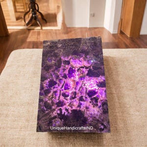 May include: A purple amethyst table top with a unique, natural pattern of crystals. The table top is lit from below, highlighting the purple hues of the amethyst.