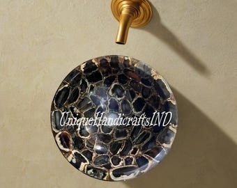 Op de afbeelding: Een ronde, zwart en bruine agaatstenen wastafel met een gouden kraan erboven. De wastafel is gemaakt van natuurlijke agaat en heeft een uniek, organisch patroon. De tekst "Unique Handicrafts IND" is zichtbaar op de wastafel.