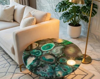 May include: A round coffee table with a unique agate stone top in shades of green, gray, and white. The table has a cylindrical base and is set on a patterned rug. A gold floor lamp and a cream-colored sofa are in the background.