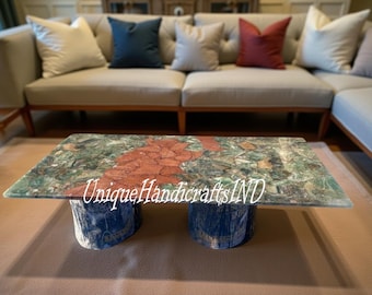 May include: A rectangular coffee table with a green and red stone top, supported by two blue cylindrical bases. The table is in front of a beige sectional sofa with decorative pillows. The text "Unique Handicrafts IND" is visible.