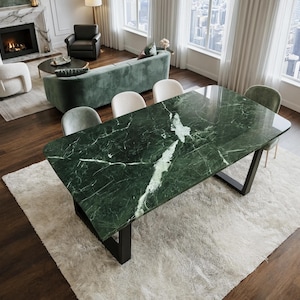 Pode incluir: Uma mesa de jantar retangular com um tampo de mármore verde escuro polido com veios brancos proeminentes. A mesa é sustentada por duas pernas robustas de metal preto em forma de U, proporcionando uma base estável para a superfície de pedra.