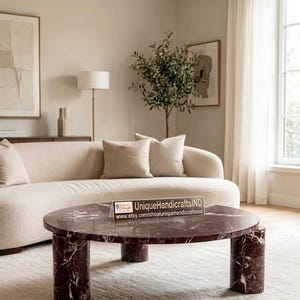 May include: A round coffee table made of dark burgundy marble with white veining, featuring three thick cylindrical legs. A clear acrylic sign on the table displays the text UniqueHandicraftsIND and the URL www.etsy.com/shop/uniquehandicraftsind.