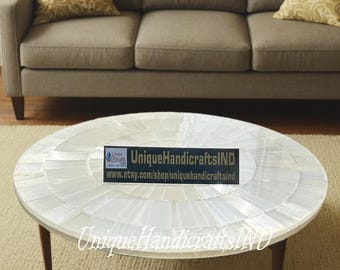 May include: A round white coffee table with a unique design made of mother of pearl tiles. The table has a dark wood base with four legs. The table is 36 inches in diameter.