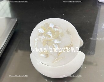May include: White marble coaster with a floral design made of mother of pearl. The coaster is round and has a raised edge. The floral design is a single flower with a stem and leaves. The coaster is made by UniqueHandicraftsIND.