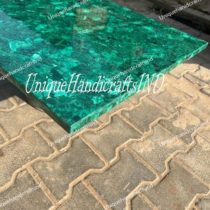 May include: A green malachite table top with a unique pattern. The table top is made of natural stone and has a polished finish. The text "Unique Handicrafts IND" is visible on the table top.