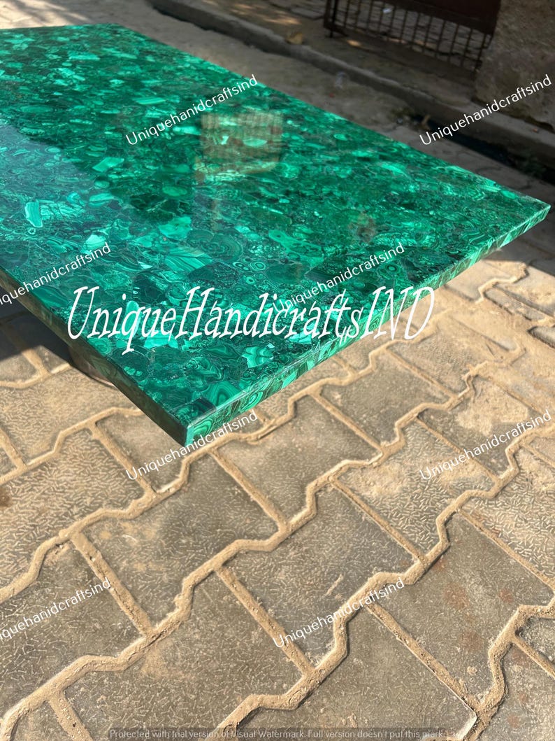 May include: A green malachite table top with a unique pattern. The table top is made of natural stone and has a polished finish. The text "Unique Handicrafts IND" is visible on the table top.