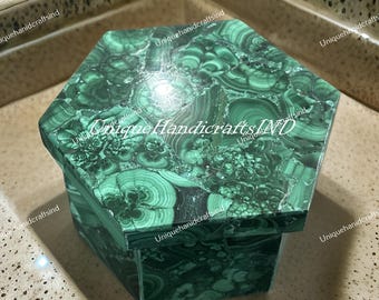 May include: A hexagonal malachite box with a lid. The box is a deep green colour with swirling patterns and textures. The words "Unique Handicrafts IND" are printed on the box.