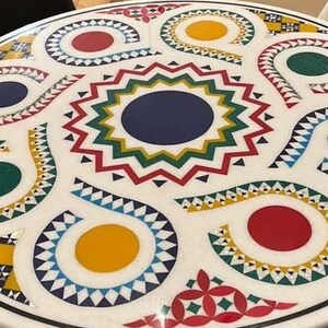 Puede incluir: Una mesa redonda blanca con un dise&ntilde;o geom&eacute;trico colorido. El dise&ntilde;o presenta c&iacute;rculos, espirales y estrellas rojas, amarillas, azules, verdes y blancas.
