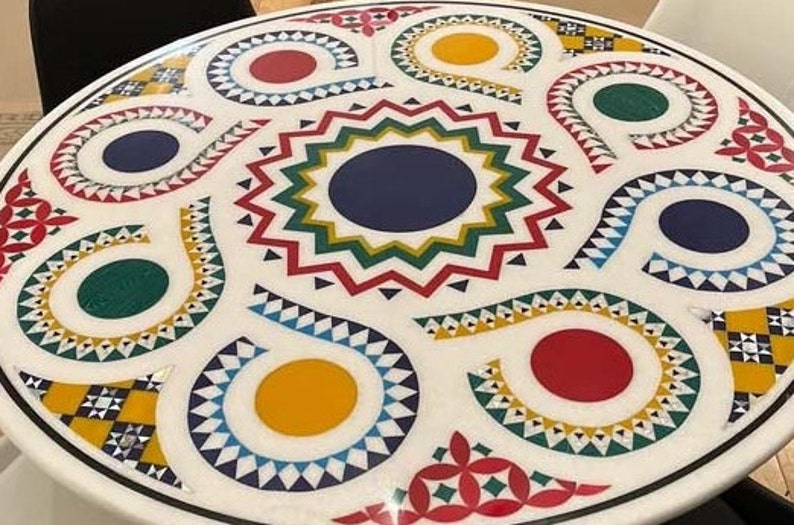 Puede incluir: Una mesa redonda blanca con un dise&ntilde;o geom&eacute;trico colorido. El dise&ntilde;o presenta c&iacute;rculos, espirales y estrellas rojas, amarillas, azules, verdes y blancas.