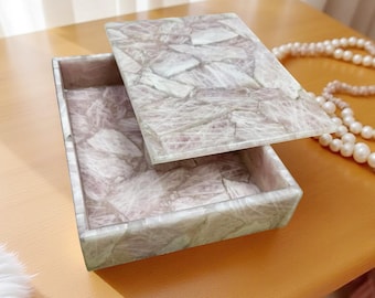 May include: A rectangular, light pink, decorative box with a lid made of natural stone. The box has a marbled pattern and is open, revealing the interior.