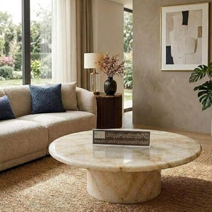 May include: A round coffee table made of polished beige stone with natural veining and a cylindrical base. A clear acrylic sign on the table displays the text UniqueHandicraftsIND and www.etsy.com/ehop/uniquehandicraftsind.