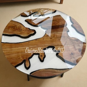 Può includere: Tavolo da caffè rotondo in legno con piano in resina epossidica bianca. La resina presenta linee nere che creano un design a forma di fiume. Il tavolo ha una base in metallo nero. Il testo "UniqueHandicraftsIND" è visibile sul piano del tavolo.