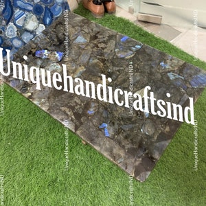 May include: A close-up of a dark blue and grey stone table top with iridescent blue flecks. The table top is made of labradorite, a type of feldspar. The table top is surrounded by green grass.