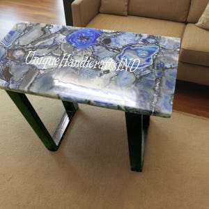 May include: A blue agate table top with a unique pattern and black metal legs. The table top is polished and has a glossy finish. The text "Unique Handicrafts IND" is visible on the table top.