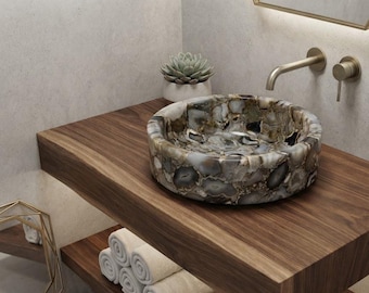 May include: A round vessel sink crafted from polished agate stone featuring a mosaic of grey, brown, and white banded patterns. The sink is mounted on a thick, dark wood floating vanity shelf with a wall-mounted brushed gold faucet and handle.