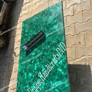 May include: A green malachite table top with a unique pattern. The table top is made of natural stone and has a polished finish. The table top is surrounded by a brick wall.