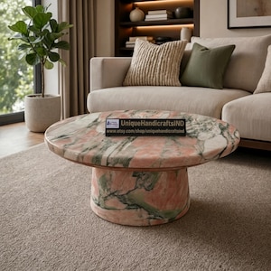 May include: A round coffee table crafted from polished stone featuring a marbled pattern of soft pink and deep green veins. The table has a wide, cylindrical base and a flat circular top. A black rectangular sign displays UniqueHandicraftsIND.
