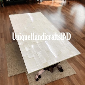 May include: A white coffee table with a unique design made of white tiles. The table has a brown metal base with ornate details. The table is sitting on a beige rug.