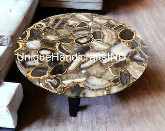 May include: Round agate coffee table with a black and gold agate top. The table has a black base and is sitting on a light gray rug.