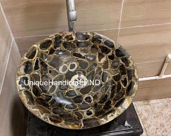 May include: A round agate sink with a brown and black agate pattern. The sink is mounted on a black countertop. The sink has a drain in the center and a faucet is visible in the background.
