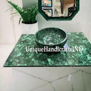 May include: A green malachite stone countertop with a matching green malachite stone sink. The countertop is rectangular and the sink is round. The text "UniqueHandicraftsIND" is visible on the countertop.
