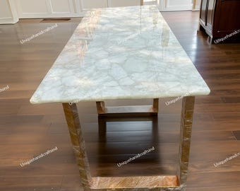 May include: A white marble table with a gold metal frame. The table has a unique, cloudy pattern and a polished finish. The table is sitting on a wooden floor.