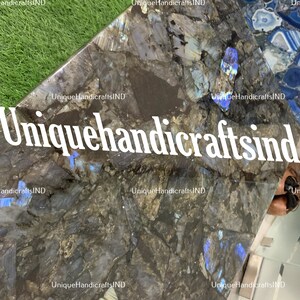 May include: A close-up of a dark grey and blue labradorite stone countertop. The stone has a unique iridescent quality, with flashes of blue and green. The countertop is ideal for a kitchen or bathroom.