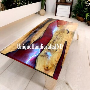 Könnte beinhalten: Ein Holz-Couchtisch mit einem roten und weißen Epoxidharzeinleger. Der Tisch hat eine natürliche Holzoptik und ein einzigartiges, fließendes Design. Der Text "UniqueHandicraftsIND" ist auf dem Tisch sichtbar.